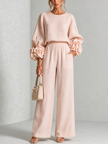 Modell i rosa set med ballongärmar, blomdetaljer och vida byxor, framifrån med handväska 1