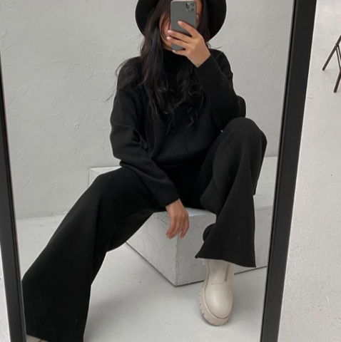 Frau in schwarzem Outfit und Hut macht Selfie im Spiegel, weiße Stiefel, modisch, modern.