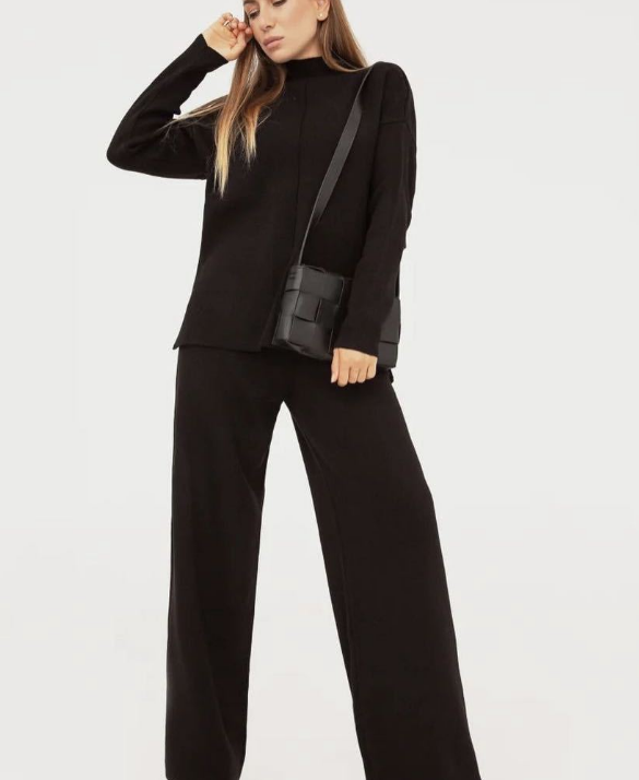 Frau in schwarzem Strickpullover und Hose, schwarze Umhängetasche, modisches Outfit.