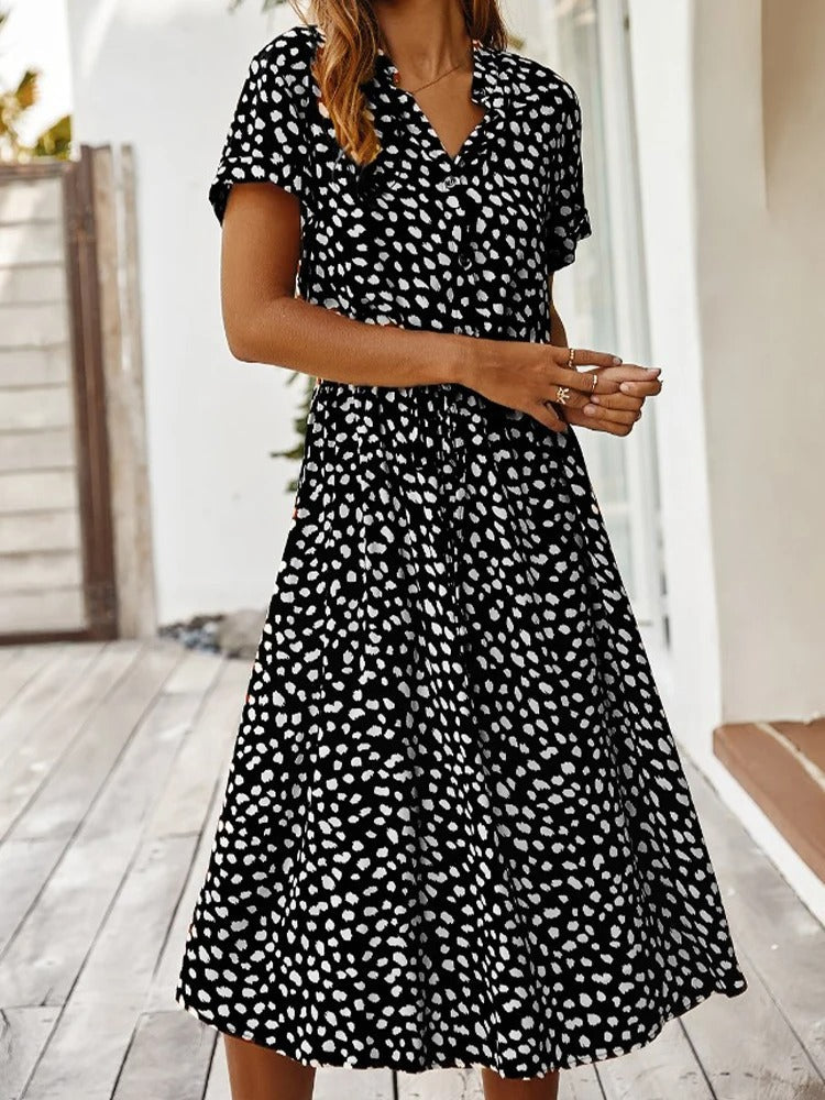 Frau in schwarz-weiß gepunktetem Sommerkleid, knielang, kurzärmelig, draußen stehend.