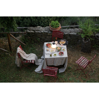 Gedeckter Gartentisch mit Speisen, roter Stuhl, Steinmauer, Abendessen im Freien, stimmungsvolle Beleuchtung.