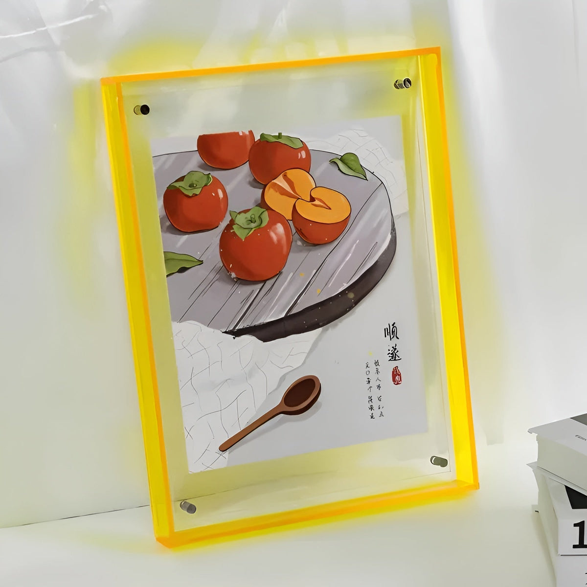 Neongul akrylram med illustration av kakifrukter på ett fat och en träsked, lutad mot en vit vägg. 12