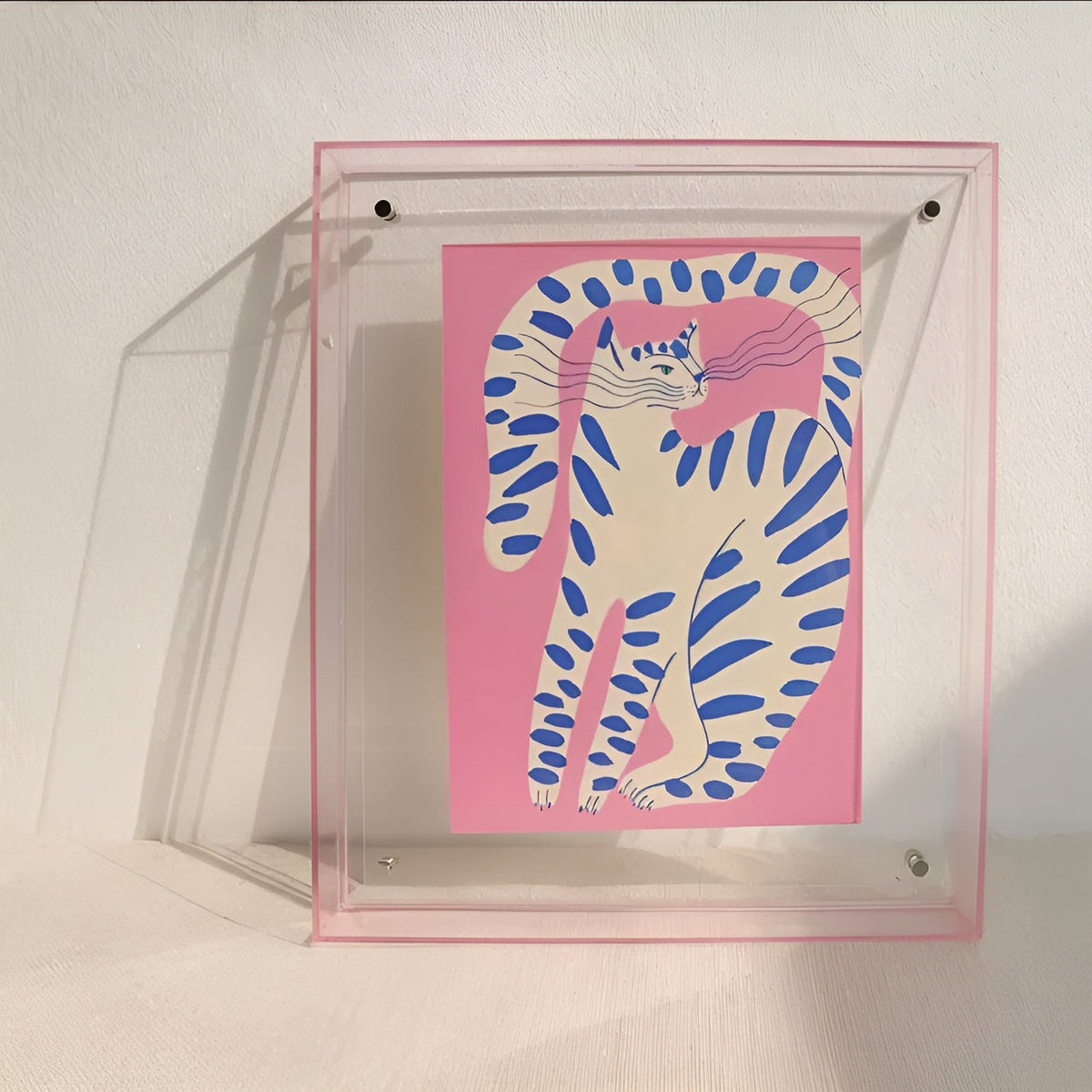 Klar akrylram med rosa kant lutad mot vit vägg, med illustration av en rosa katt med blå ränder. 9