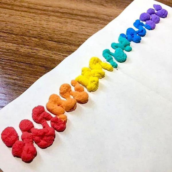 Bunte Knetmasse in Regenbogenfarben auf weißem Papier, kreative Bastelmaterialien.
