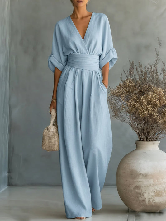 Kvinna i ljusblå jumpsuit med V-ringning och vida ben, med en flätad väska i handen 2