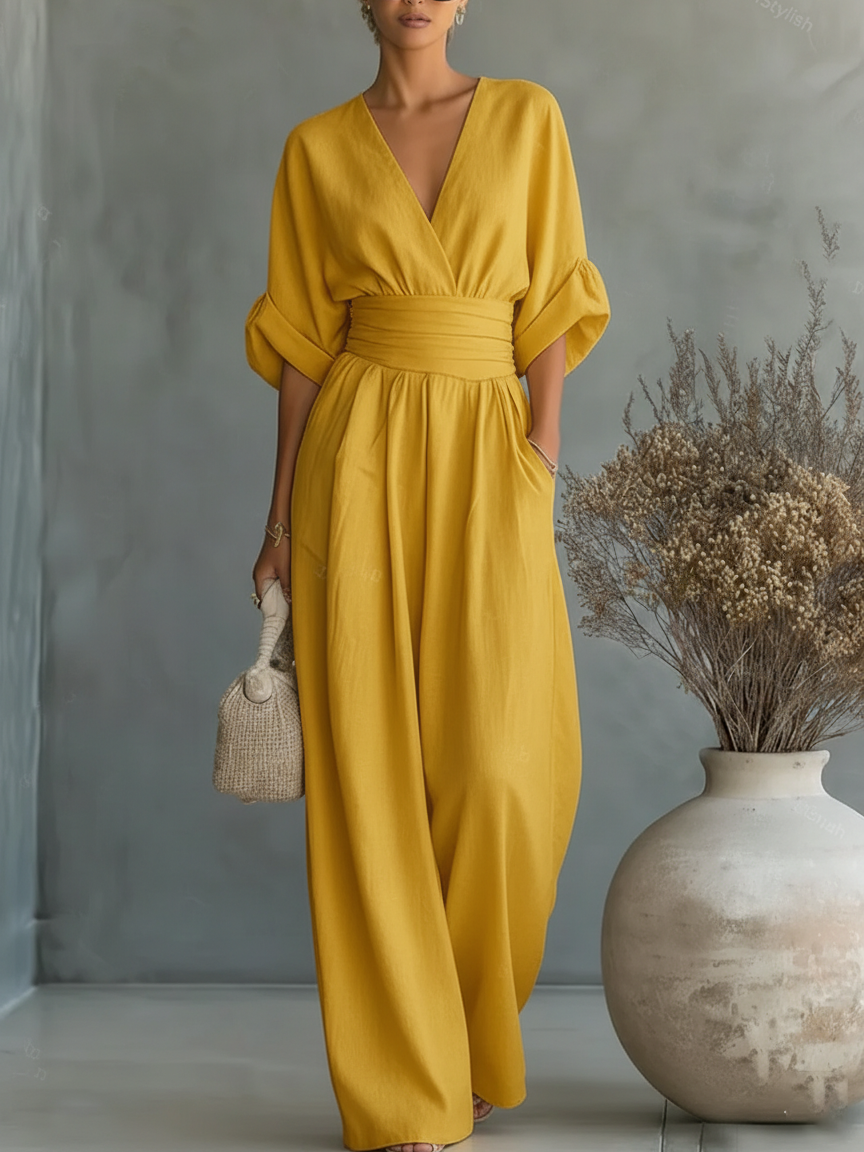 Kvinna i senapsgul jumpsuit med kimonoärmar och vida ben, med en flätad väska i handen 10