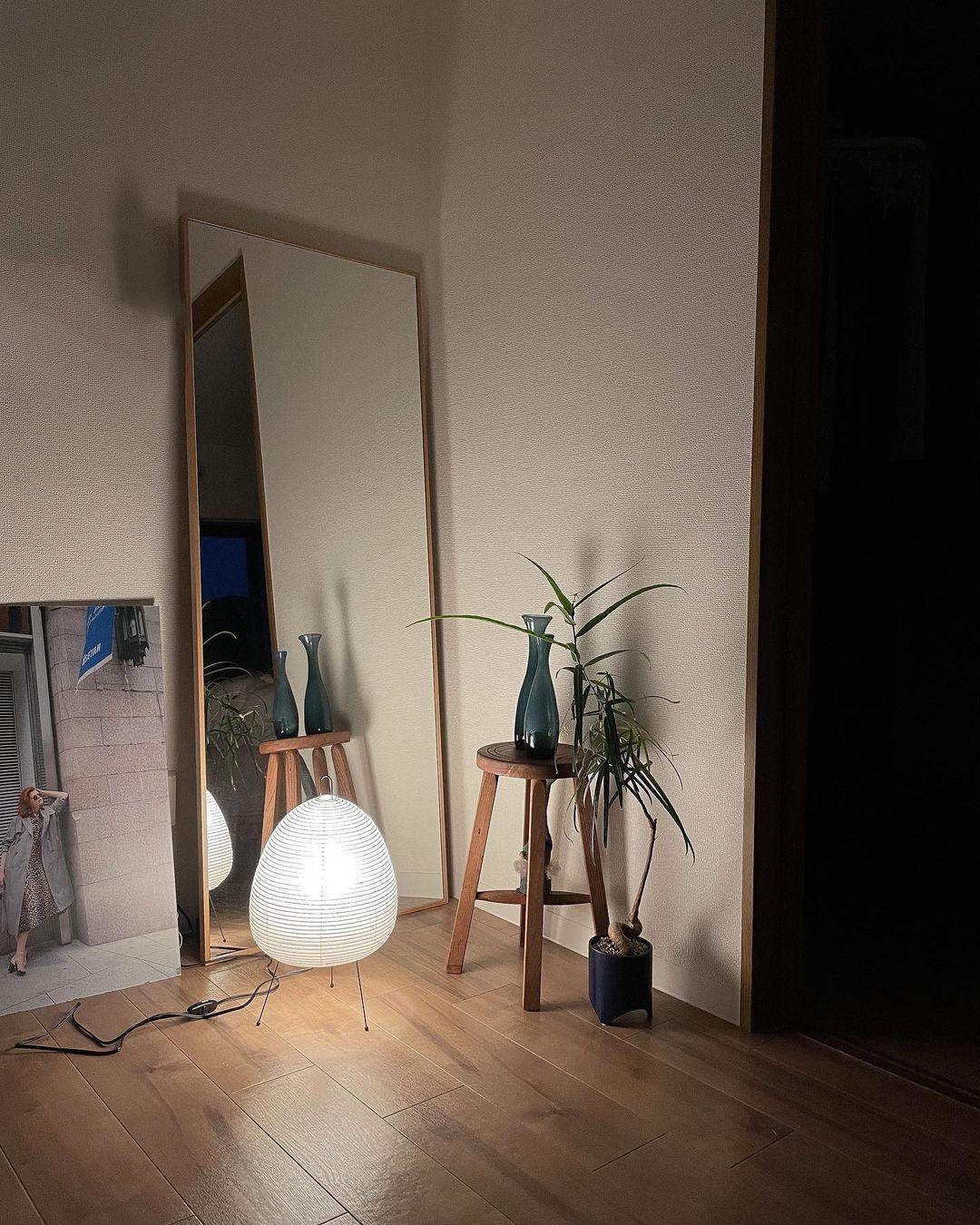 Akari Tischlampe 47, weiß, Papier, beleuchtet, neben Holzstuhl und Pflanze, modernes Design.
