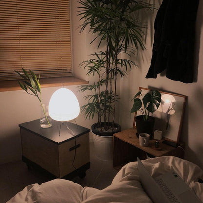 Akari Tischlampe, weiß, modern, beleuchtet, neben Zimmerpflanzen, gemütliches Schlafzimmer.