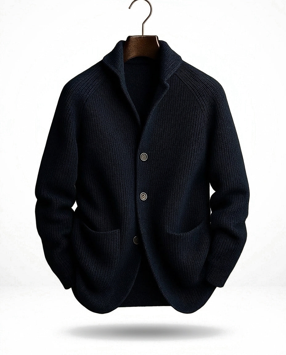 Marinblå kofta på träbygel sedd framifrån, med ribbstickat mönster, sjalkrage, knappar och två fickor. 3