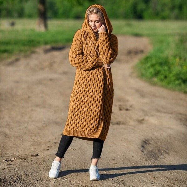 Frau in braunem, gestricktem Cardigan mit Kapuze, draußen auf einem Feldweg.