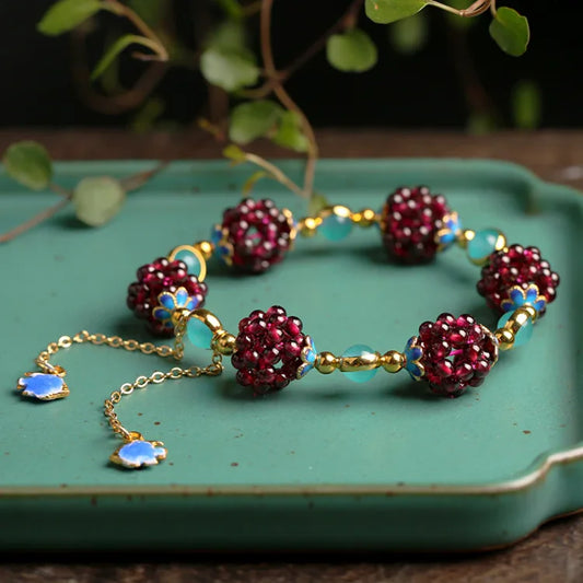 Goldene Armband mit roten Perlen und blauen Akzenten auf grünem Tablett, eleganter Schmuck.