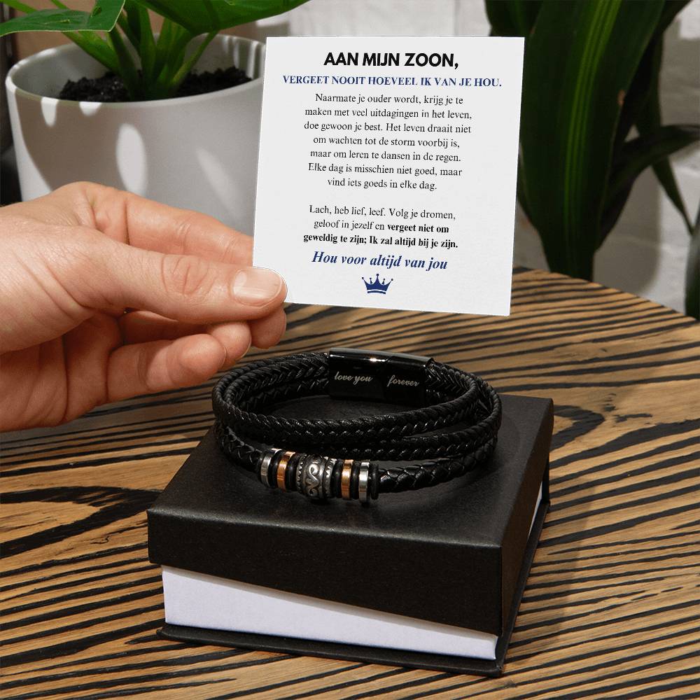 Schwarzes Lederarmband mit Metallakzenten auf Holztisch, Geschenkbox und Karte im Hintergrund.
