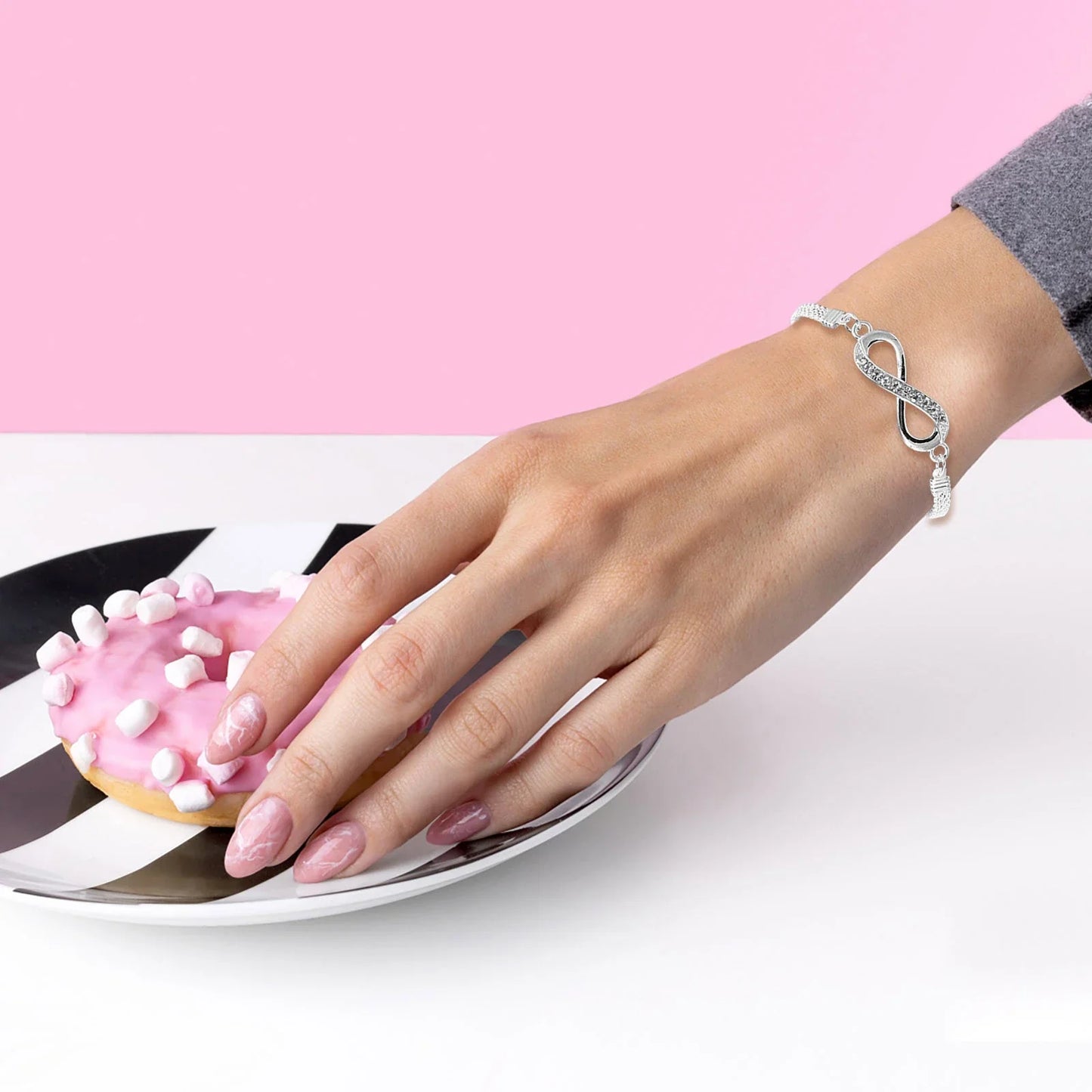 Silberarmband mit Unendlichkeitssymbol, Damenhand, rosa Donut, stilvoll, modisch, Geschenkidee.
