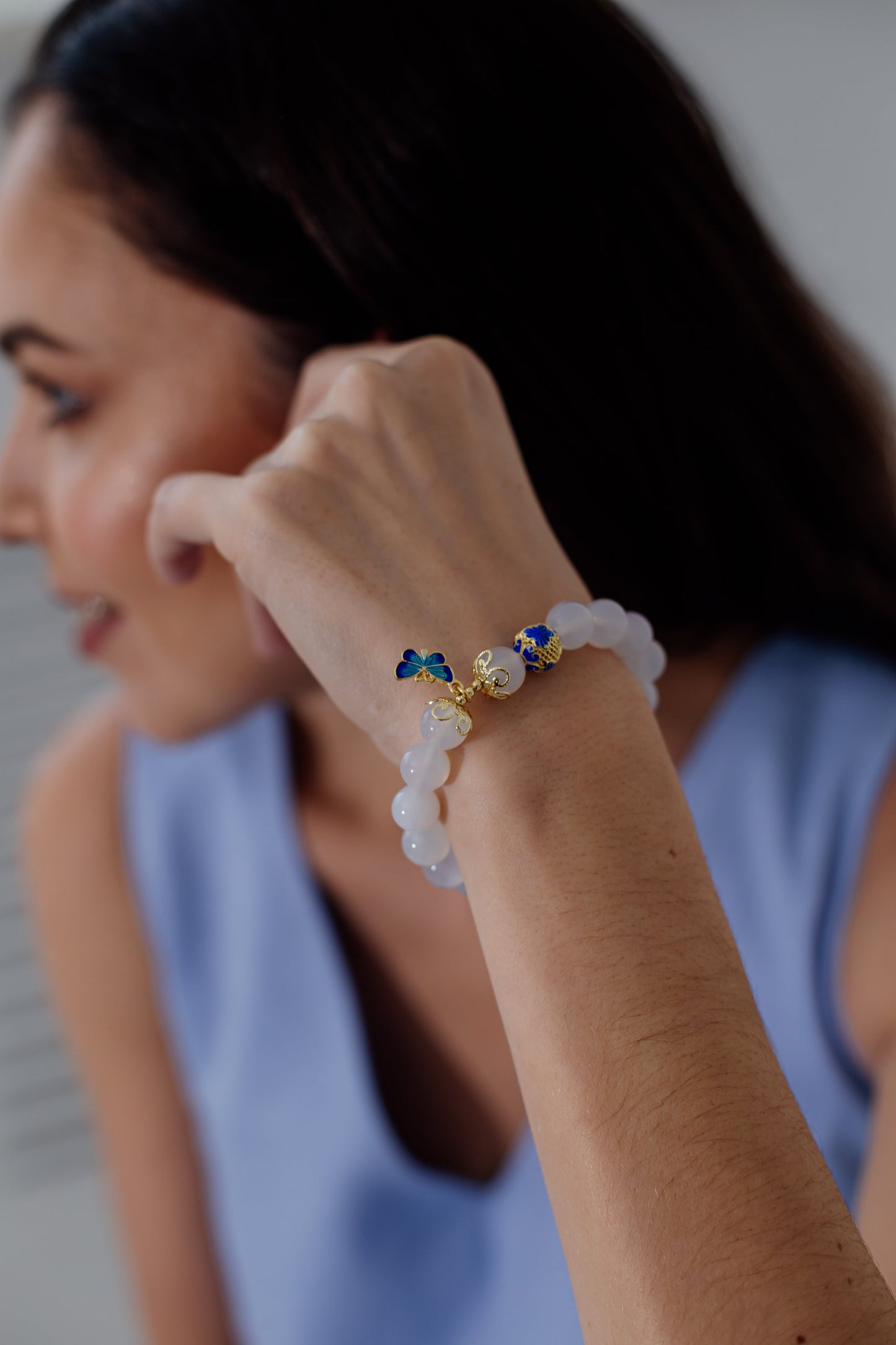 Frau mit weißem Perlenarmband, goldene Schmetterlingsdetails, elegantes Schmuckdesign.