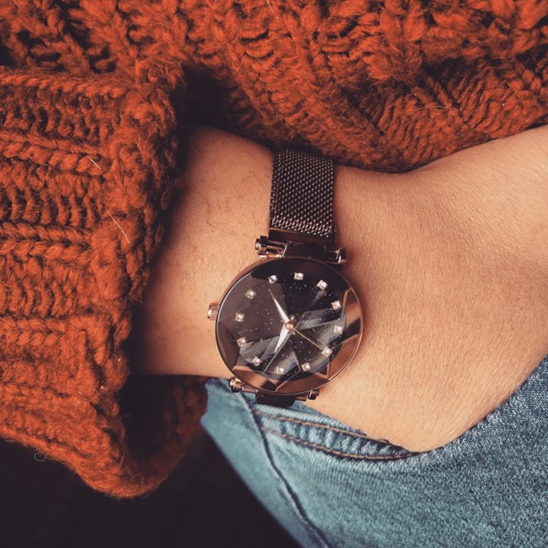 Armbanduhr mit schwarzem Zifferblatt und Metallarmband, getragen auf gestricktem Pullover.