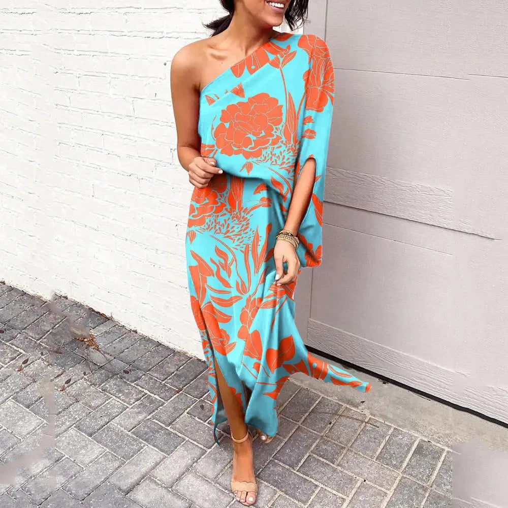 Frau in blau-orange asymmetrischem Kleid mit Blumenmuster, lächelnd, auf Gehweg stehend.