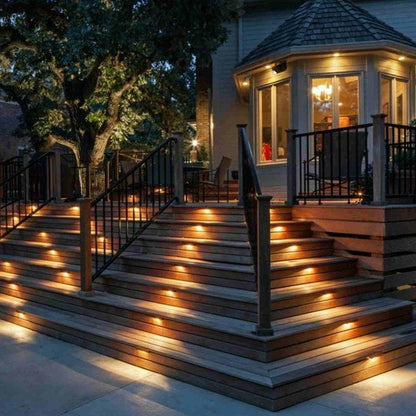 Beleuchtete Holzterrasse mit Stufen, LED-Lichtern, schwarzem Geländer, abends, Haus im Hintergrund.
