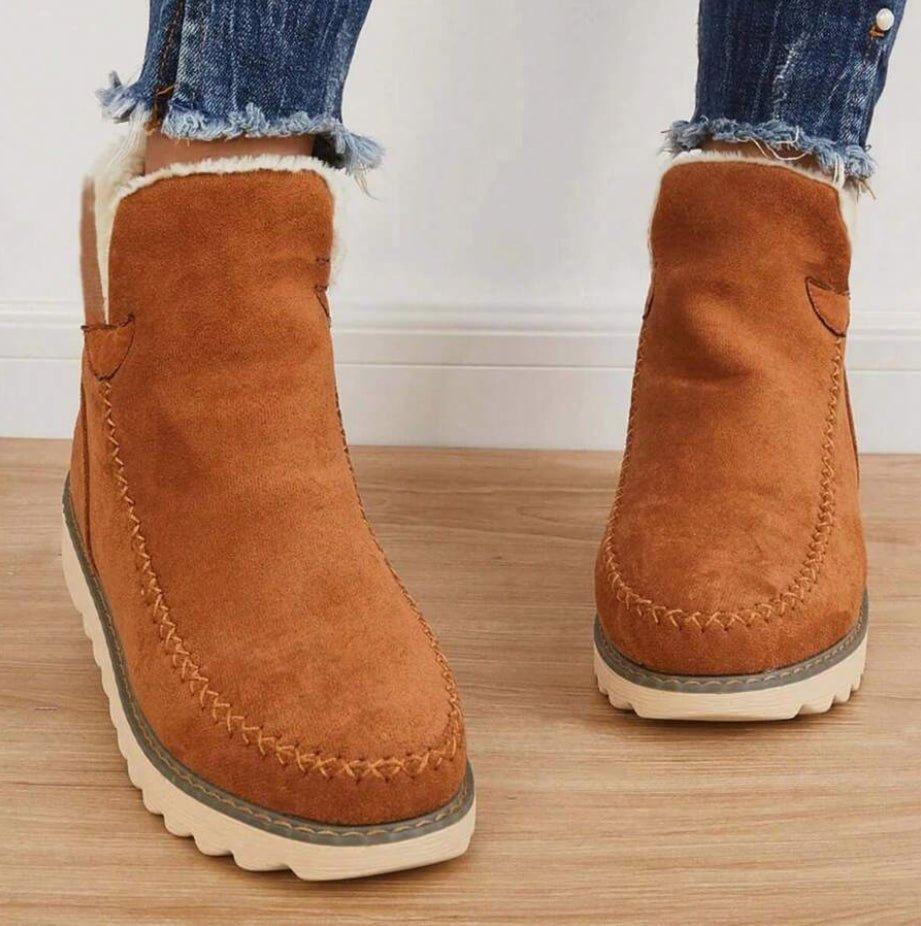 Närbild framifrån på bruna vinterboots med dekorativ kryssyckel på tån och vit fleecefoder i skaftet, bärs med jeans. 5