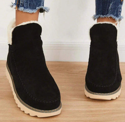 Svarta vinterboots sedda framifrån på en modell, med tjock vit fleecefoder i skaftet och kraftig beige sula. 4