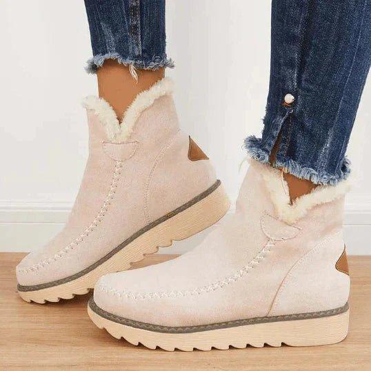 Beige ankelboots med mjuk vit fleecekant och kryssyckel längs framsidan, bärs av en modell i jeans med pärlknapp. 3