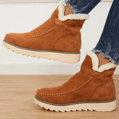 Bruna ankelboots i mockaliknande material med vit fleecekant och beige sula, sedda från sidan på en modell i jeans. 2