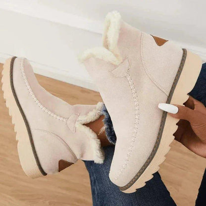 Beige boots hållna i handen av en sittande modell, med fleecefoder, små bruna detaljer på hälen och räfflad sula. 6