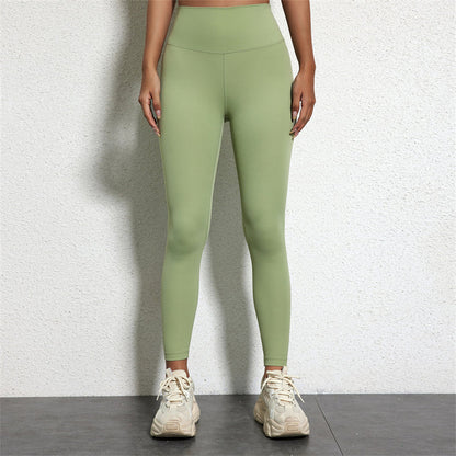 Frau in grüner Leggings und weißen Turnschuhen vor weißer Wand.