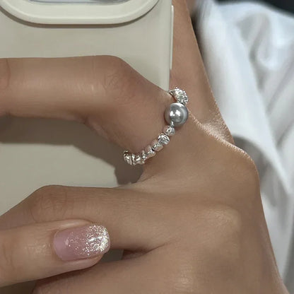 Silberner Perlenring am Finger, elegantes Schmuckdesign, glänzende Oberfläche, Damenmode.