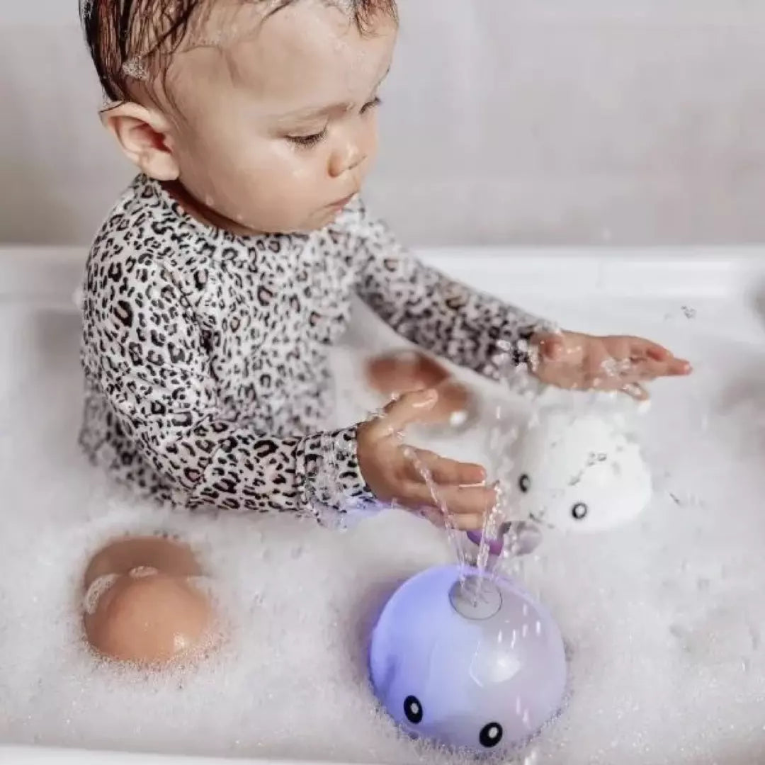 Kleinkind in der Badewanne mit leuchtendem Wal-Badespielzeug, Schaum, Leopard-Pyjama.