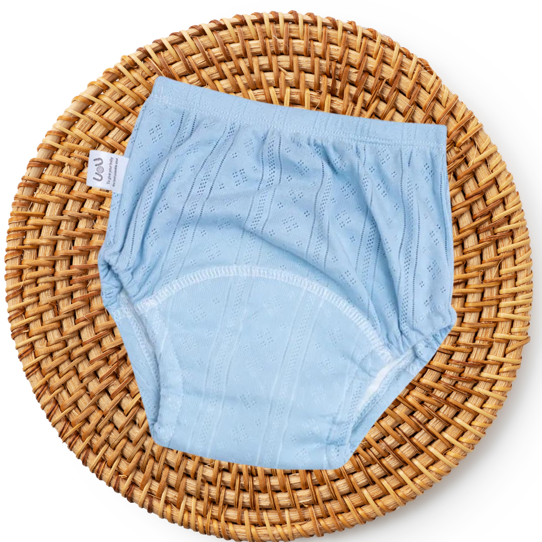 Hellblaue Baby-Unterhose aus Baumwolle auf rundem, geflochtenem Korb.