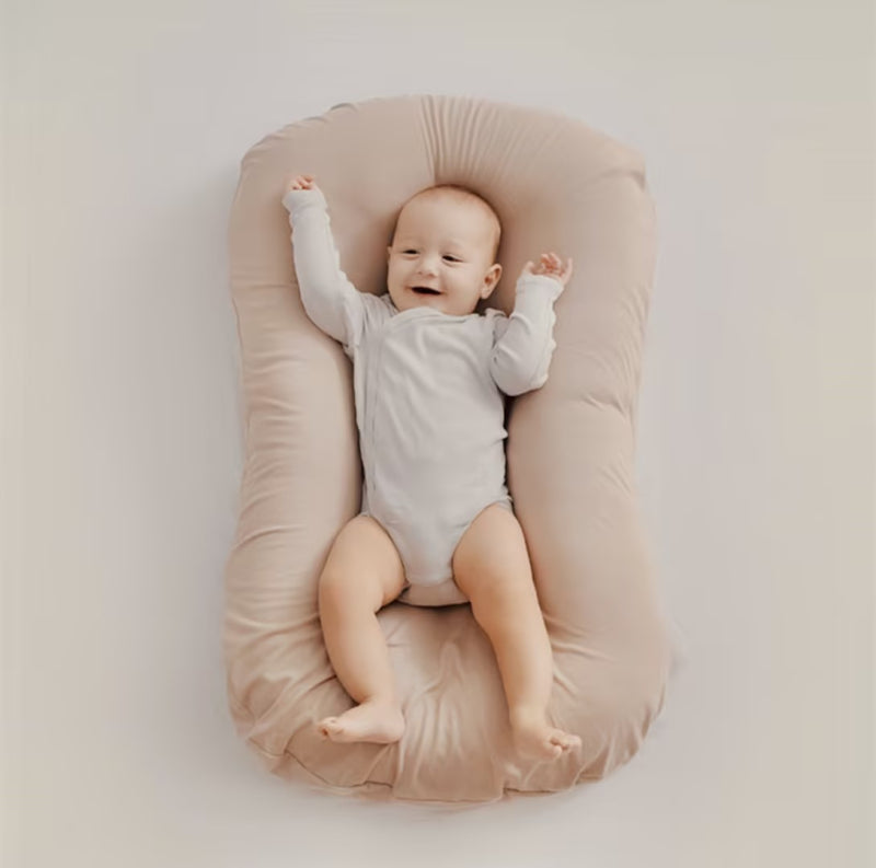 Lächelndes Baby in beigem Babynest, weicher Stoff, gemütlich, sicherer Schlafplatz.