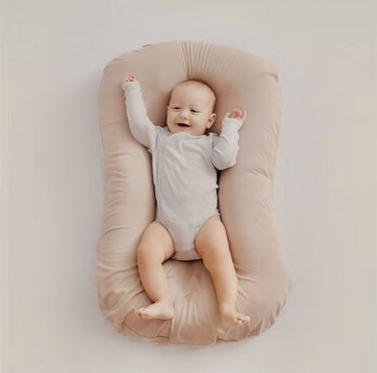 Lächelndes Baby in beigem Babynest, weich, bequem, ideal für Neugeborene, Schlafunterstützung.