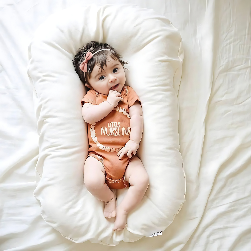 Kleinkind in orangefarbenem Strampler auf weißem Babynest, lächelnd, mit rosa Haarband.