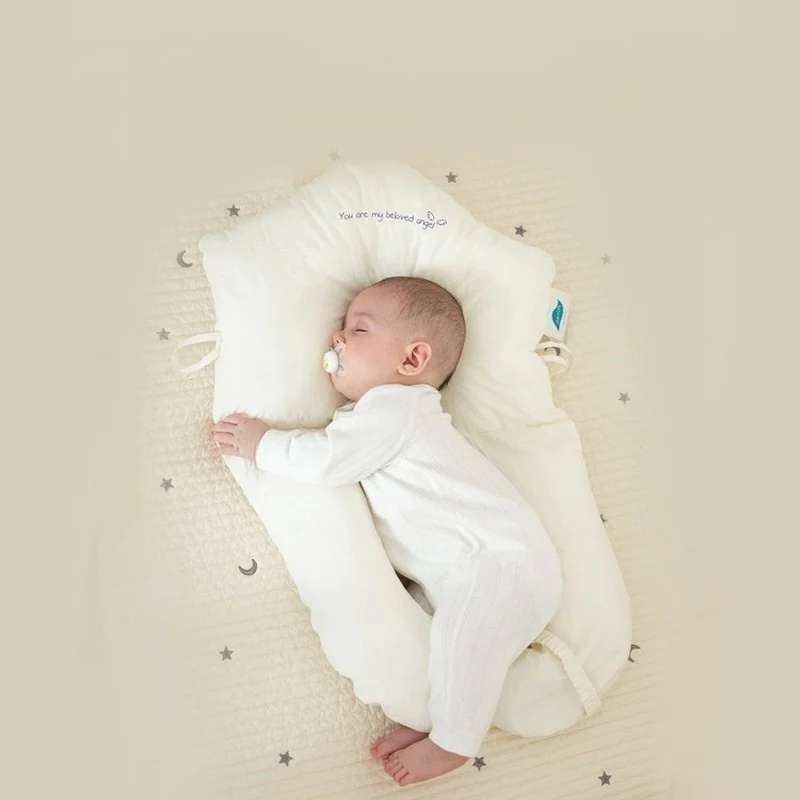 Baby schläft in weißem Babynest auf beigem Hintergrund mit Sternenmuster.