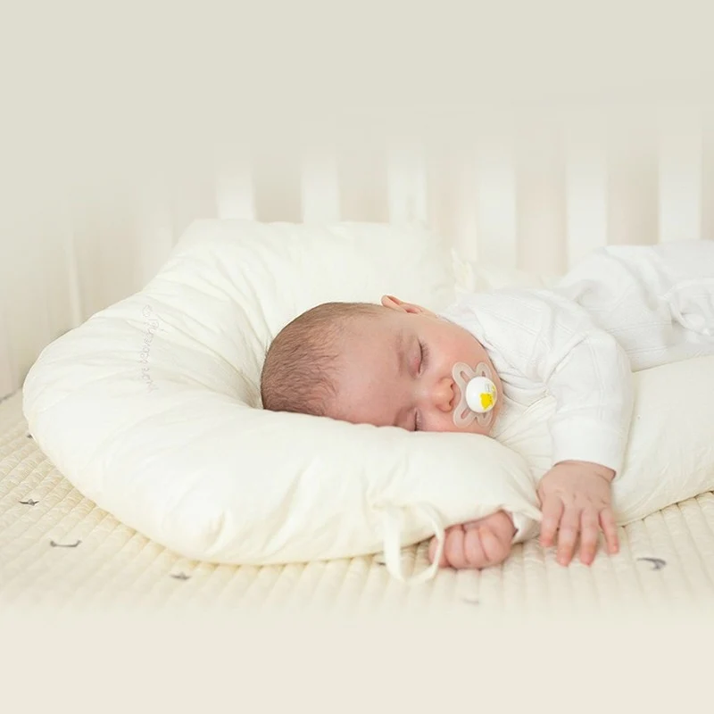 Schlafendes Baby mit Schnuller auf weißem Stillkissen im Kinderbett.