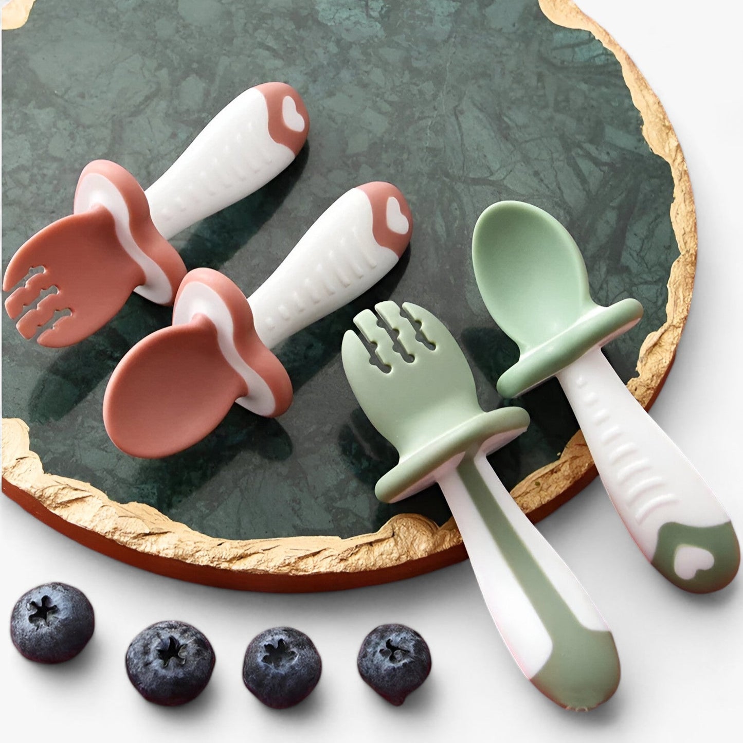 Baby Besteck Set aus Silikon in Rosa und Grün auf Marmorplatte, ergonomisch, BPA-frei.