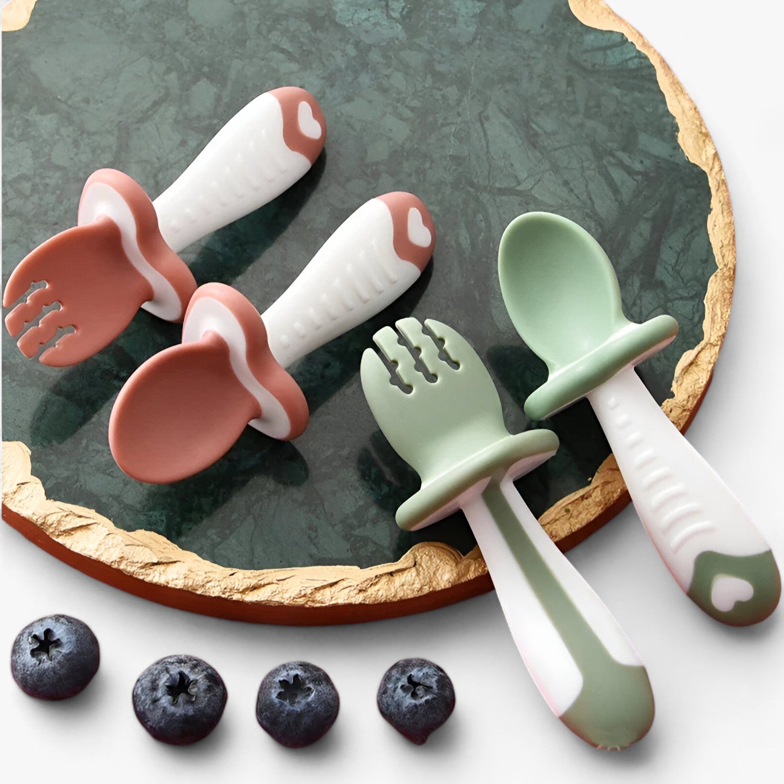 Baby Besteck Set aus Silikon in Rosa und Grün auf Marmorplatte, ergonomisch, BPA-frei.