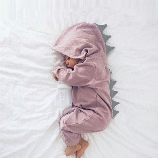 Schlafender Säugling im rosa Dinosaurier-Strampler mit Kapuze auf weißem Bett.