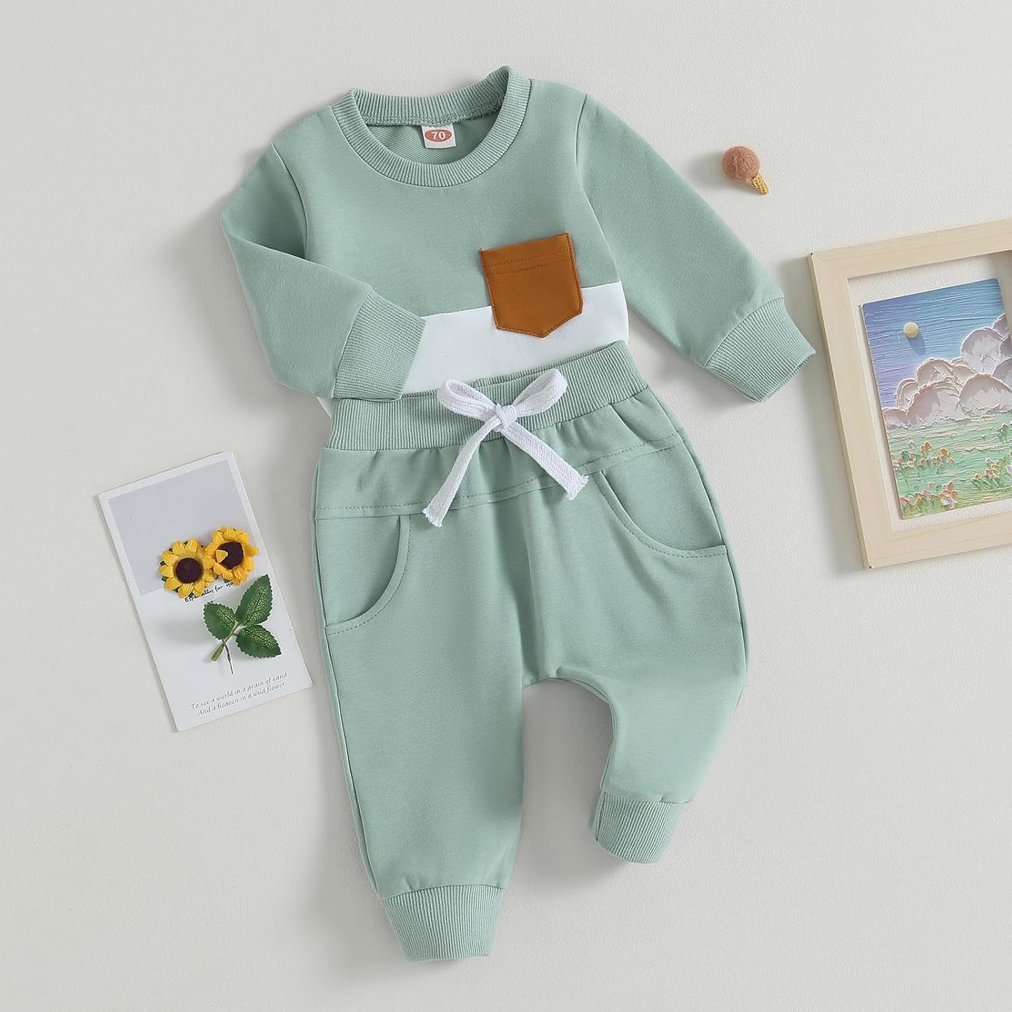 Grüner Baby-Strampler mit brauner Tasche und weißem Band, Baumwolle, langärmelig.