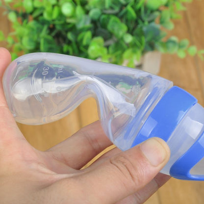 Transparente Babyflasche mit blauem Deckel, ergonomisch, Kunststoff, vor grünem Hintergrund.