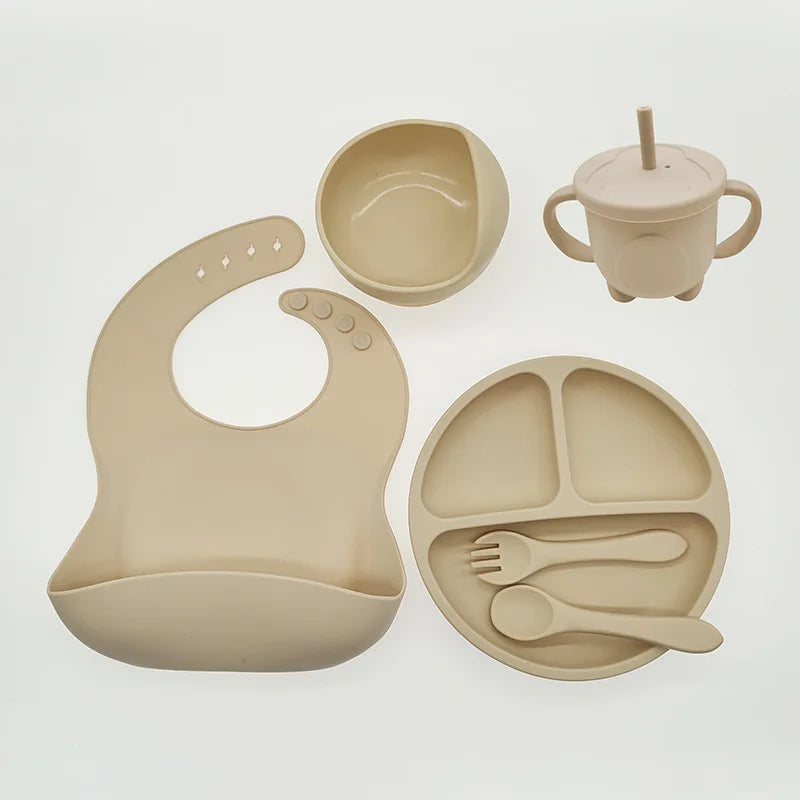 Beiges Babygeschirr-Set aus Silikon mit Lätzchen, Teller, Schüssel, Becher und Besteck.