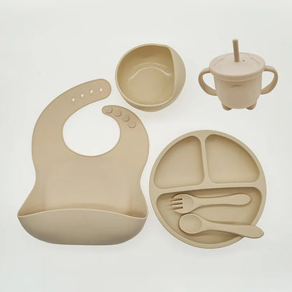 Beiges Babygeschirr-Set aus Silikon mit Lätzchen, Teller, Schüssel, Becher und Besteck.