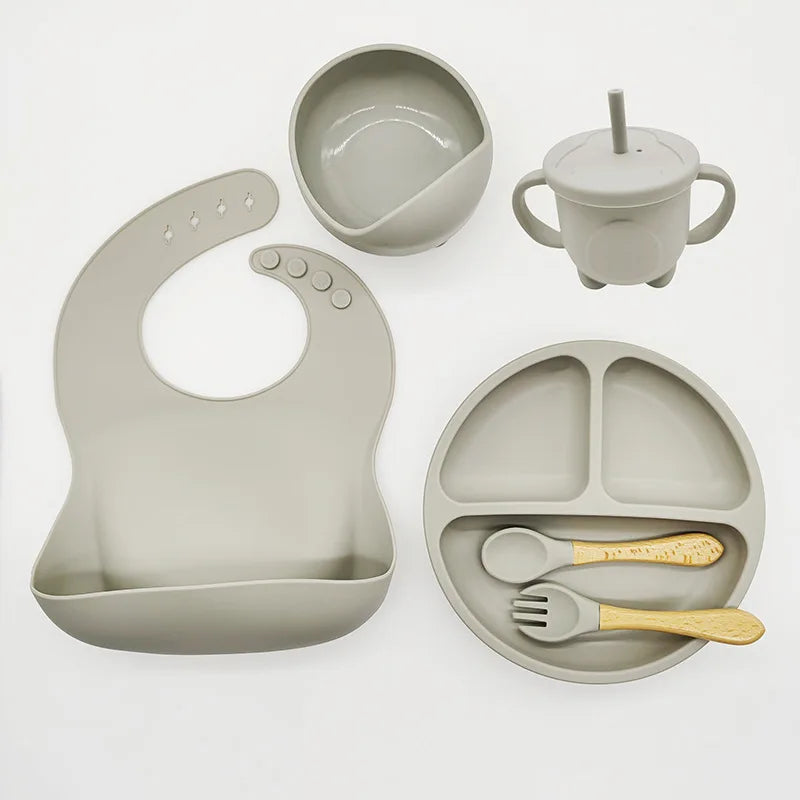 Graues Silikon-Babygeschirr-Set mit Lätzchen, Teller, Schüssel, Becher und Besteck.