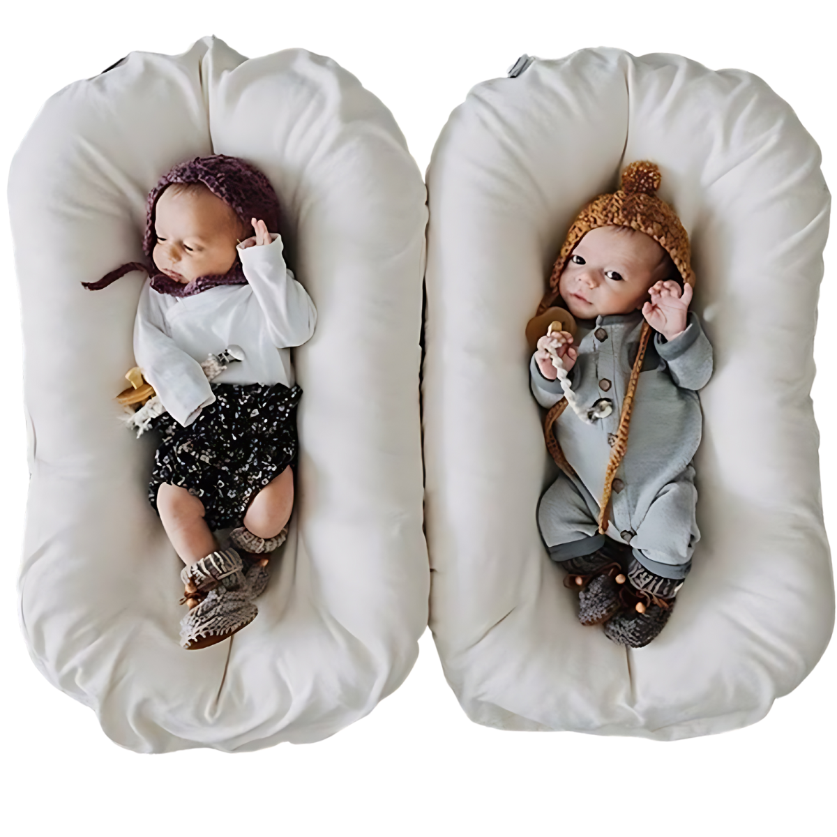 Zwei Babys in weißen Babynestern, tragen gestrickte Mützen und Strampler, auf weißem Hintergrund.