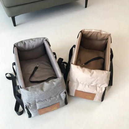 Zwei tragbare Babytragetaschen, grau und beige, mit Sicherheitsgurten auf weißem Boden.