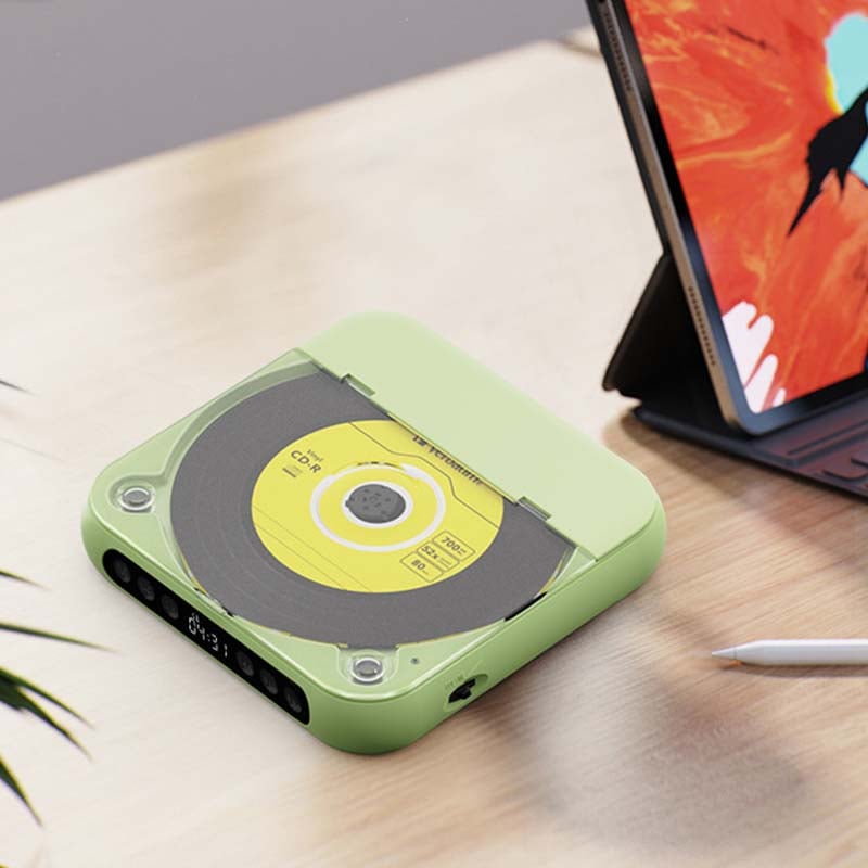 Grön CD-spelare med gul skiva sedd uppifrån på ett ljust bord, med en surfplatta och en penna intill. 12