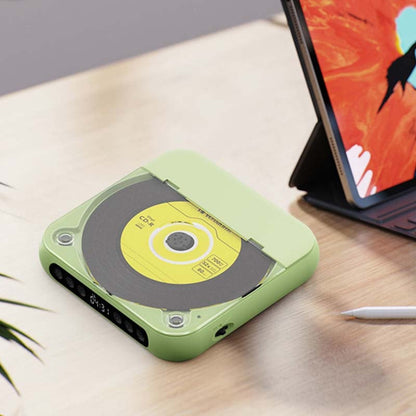 Grön CD-spelare med gul skiva sedd uppifrån på ett ljust bord, med en surfplatta och en penna intill. 12