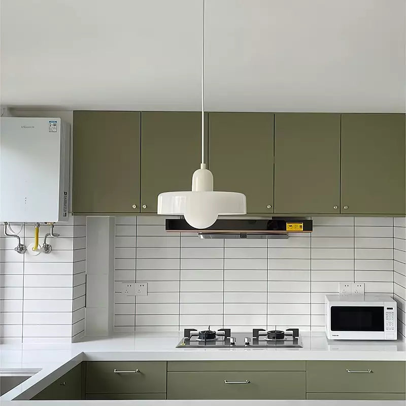 Weiße Pendelleuchte im Bauhaus-Stil über moderner Küche mit grünen Schränken und Mikrowelle.