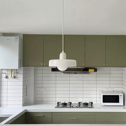 Weiße Pendelleuchte im Bauhaus-Stil über moderner Küche mit grünen Schränken und Mikrowelle.