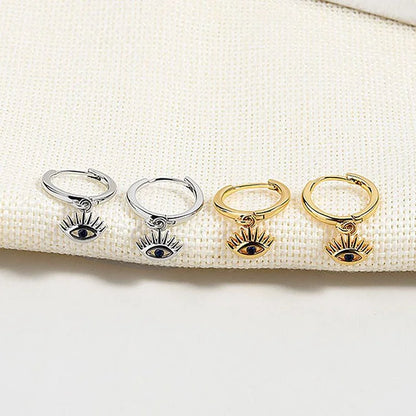 Silberne und goldene Ohrringe mit Auge-Anhänger auf beigem Stoff, modischer Schmuck.